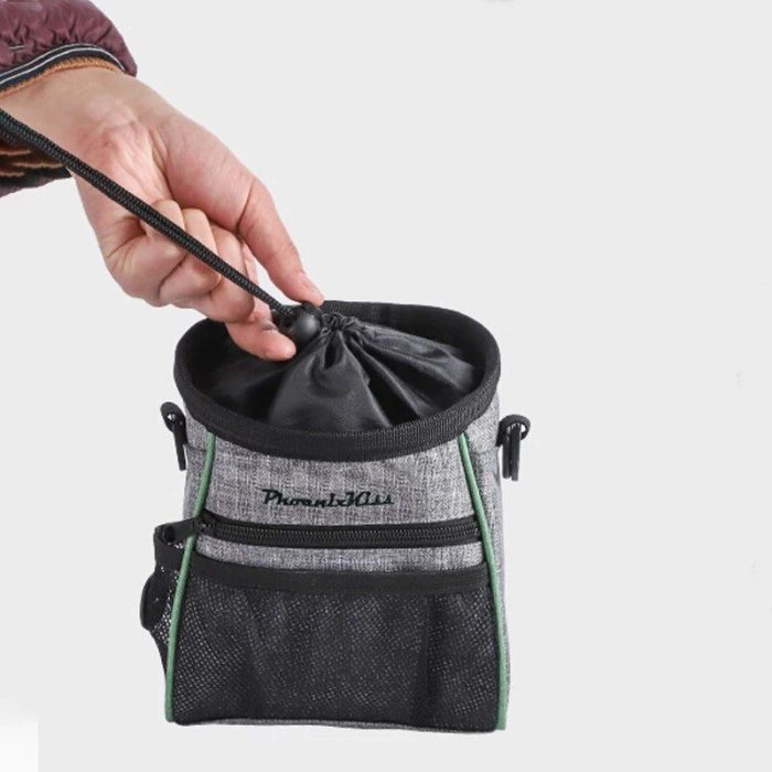 A hand is holding a black drawstring of a gray and black fabric pouch with pockets and the word "10113-edca74.jpg" on it, set against a plain background. Ideal as a multi-functional snack bag for dog training, it keeps treats and essentials organized.