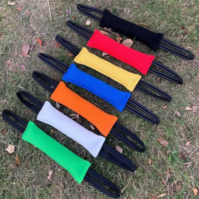 Seven brightly colored tug toys are laid out on grass, each with a black handle. Ideal for dog training, 10126-a18f61.jpg comes in red, yellow, orange, white, green, blue, and black. Perfect for molar grinding and teeth cleaning while your pup plays!