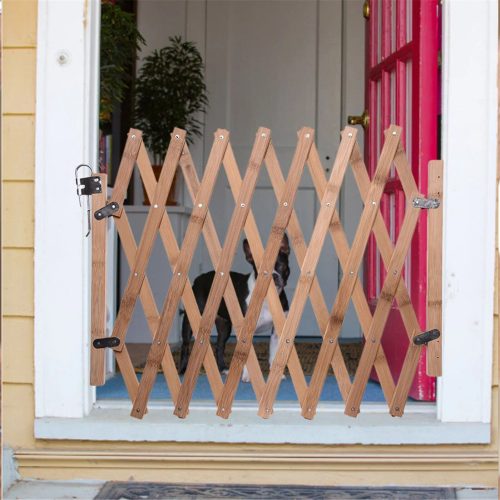 A 10160-aa9c42.jpg, resembling an adjustable bamboo pet safety gate, is installed in a doorway with a pink doorframe, preventing a small black and white dog from passing through.