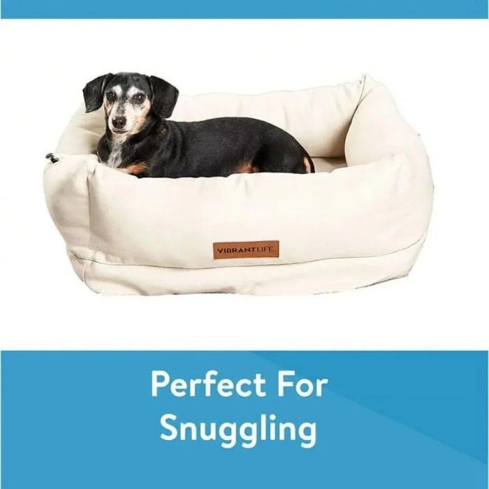 A small black and tan dog lies comfortably on a white plush 10199-1609bf.jpg labeled "Vibrant Life," with text below reading "Perfect For Snuggling.