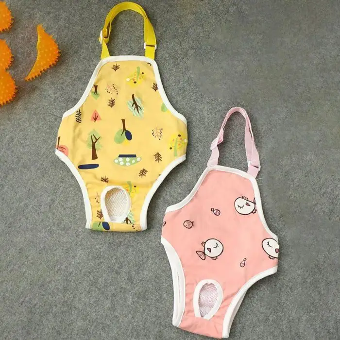 Two colorful dog harnesses on a grey surface; one is yellow with a forest pattern, and the other is pink with animal faces. Both have leg holes and buckled straps. An orange spiky toy sits nearby. Ideal for pairing with a 10445-96181c.jpg for complete outdoor adventures!