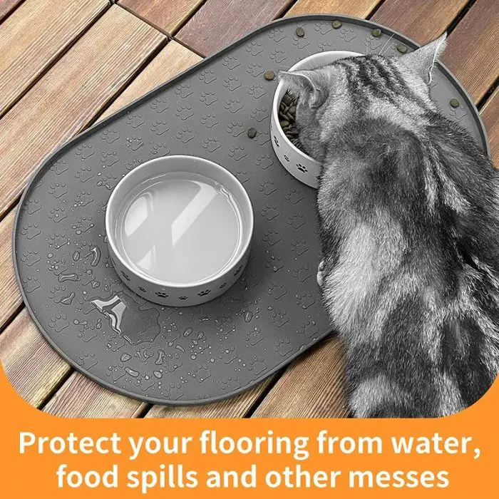 A cat eats from a bowl on a gray pet feeding mat with another bowl of water. The mat is on a wooden floor with text below reading, "Protect your flooring from water, food spills, and other messes. 10573-d7fc9f.jpg