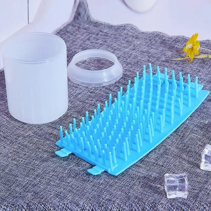 A 10610-e4a2db.jpg, its lid, and a blue silicone Paw Plunger ice tray with protruding spikes are placed on a gray fabric surface.