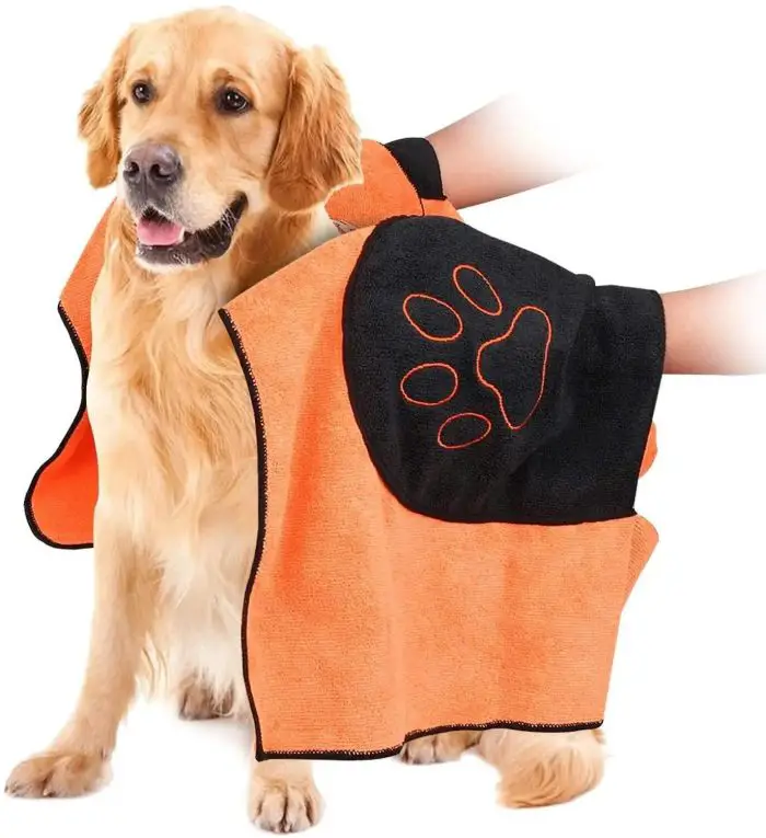 A dog is dried with an orange and black 10661-8a12ef.jpg featuring a paw print design. Two human arms hold the towel around the dog.