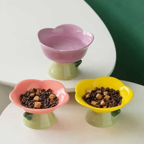 Three 10869-493ffb.jpg sit on a white surface. One purple bowl is empty, while the pink and yellow bowls are filled with brown kibble and small yellow chunks.