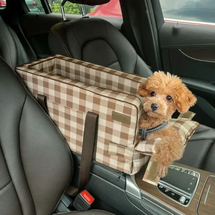 A small brown dog sits in a plaid, waterproof 11079-9eae6d.jpg secured to the passenger seat of a car.