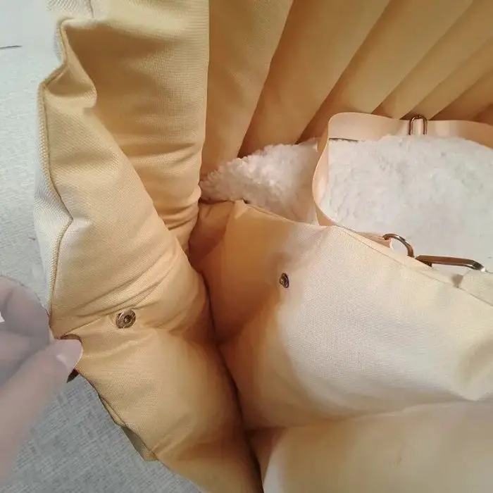 Close-up of a beige fabric bag with metallic snaps and a cream-colored, fluffy interior lining, resembling the cozy interior of 11097-beb223.jpg. A hand is holding the edge of the fabric near one of the snaps.