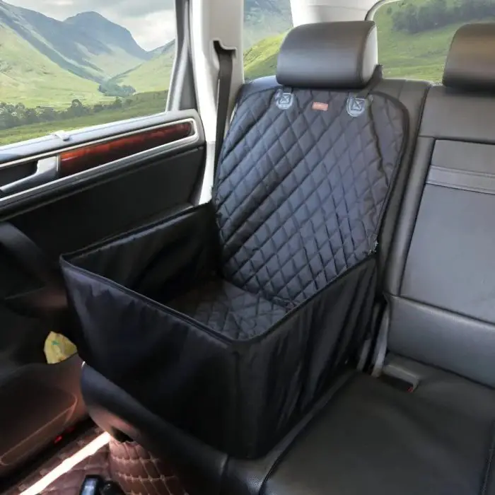 View of a black quilted 11102-2e3c31.jpg designed for pet protection, positioned on the back seat of a car, with green hills and mountains visible through the windows.