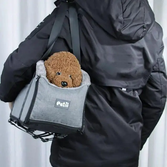 A person in a black jacket is carrying a small brown dog in a 11110-a45d6e.jpg, resembling a cozy booster seat.