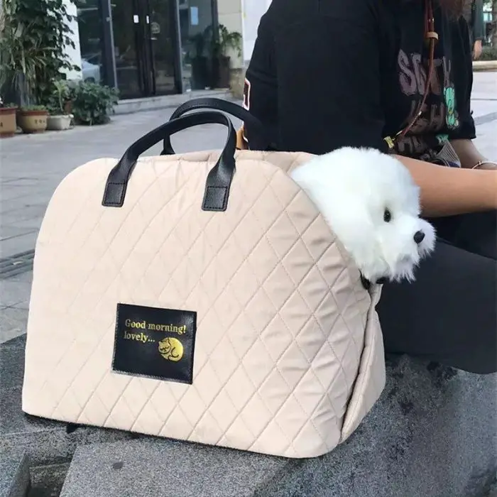 A small white dog, the perfect cozy companion, peeks out of a beige quilted handbag with black handles. The bag has a patch that reads "Good morning lovely" alongside a small yellow crescent moon (11115-4a107c.jpg).