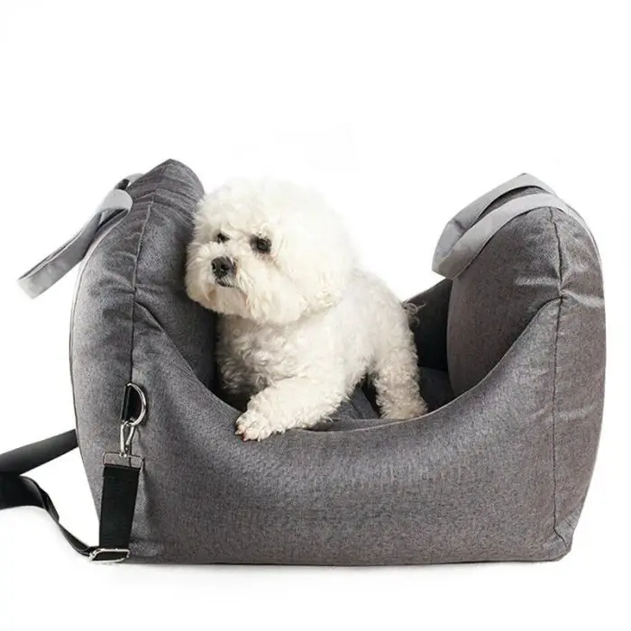 A small, fluffy white dog sits comfortably in a gray 11119-189451.jpg, secured with straps and a seatbelt clip.