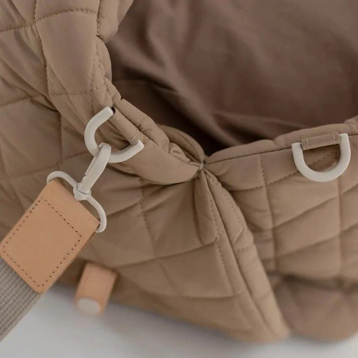 Close-up of a beige, quilted 11126-28a1b0.jpg with a clasp and strap detail in a matching tone. The bag appears to be made from a soft, padded material.