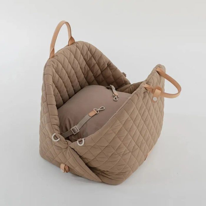 A tan-colored, quilted fabric baby carrier with tan leather handles and securing straps, sitting on a white background could effortlessly double as a stylish 11126-b9c5ef.jpg.