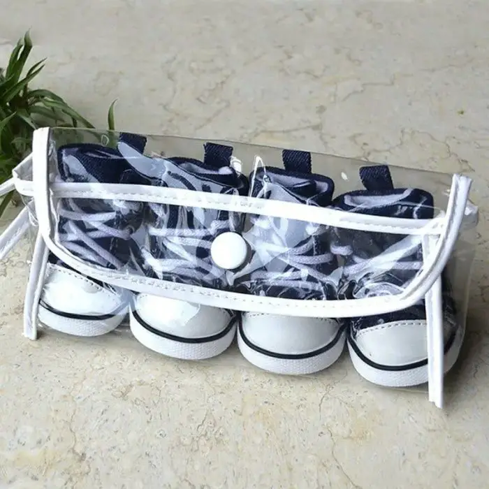 Transparent case containing two pairs of small dog sport shoes with navy and white laces and soles, placed on a beige surface next to green foliage. Product Name: 11821-ccbebf.jpg