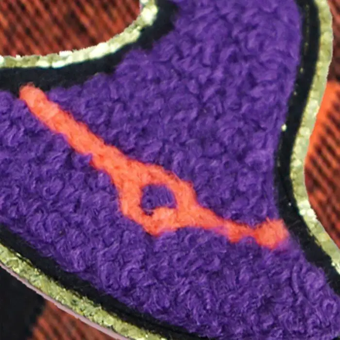 In the foreground, a detailed view showcases a section of the 11881-5cbf44.jpg bandana, featuring a purple textured fabric accented with a horizontal orange design outlined in both black and gold. The blurred background highlights striped patterns blending shades of brown and orange.