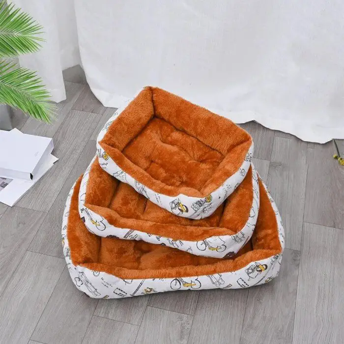 Three plush pet beds from the product 12442-74465a.jpg are stacked on top of each other. They are rectangular in shape and come in different sizes, featuring vibrant orange interiors and white exteriors adorned with a playful cartoon pattern. The neatly stacked beds rest on a wooden floor beside a small green plant.