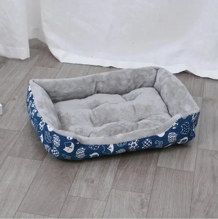 A rectangular pet bed, identified by product name 12442-98e2c9.jpg, showcases a blue outer fabric adorned with white patterns and boasts a gray, cushioned interior, all set upon a wooden floor.