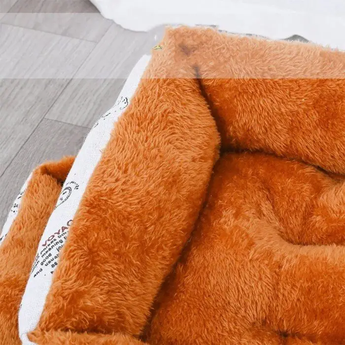 Close-up of product 12442-f5695b.jpg, a plush orange pet bed on a wooden floor. The bed features soft, fluffy fabric and a cushioned interior, offering a cozy space for pets. The edge of a white cloth is visible in the background.