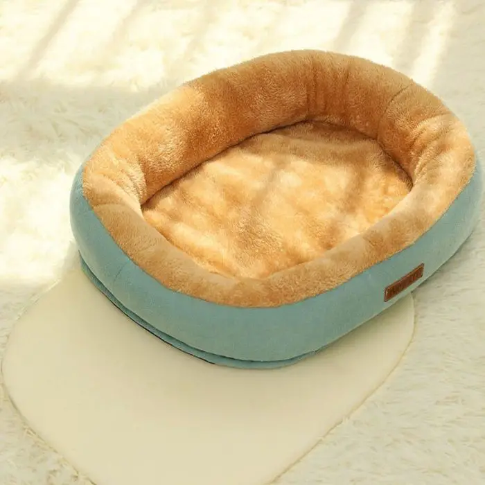 A small, plush pet bed featuring a light brown interior and blue exterior sits on a white, shaggy rug in a sunlit room, perfect for your furry friend. Product Code: 12447-f9d9eb.jpg.