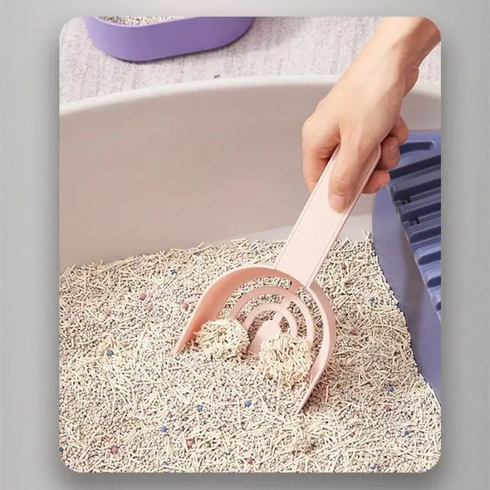 A hand is shown using the 12584-5fde75.jpg pink scoop to remove clumps from a self-cleaning litter box filled with granular litter.