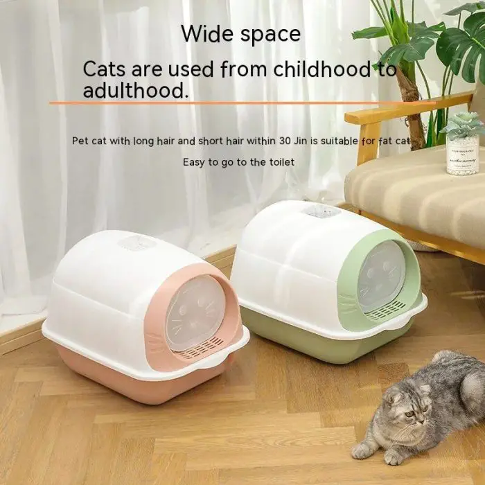 Two covered cat litter boxes, one pink and one green, are placed on a wooden floor next to a gray cat. The text above highlights the spacious design and suitability for cats from kittenhood to adulthood. Image file name: 12586-a3938b.jpg