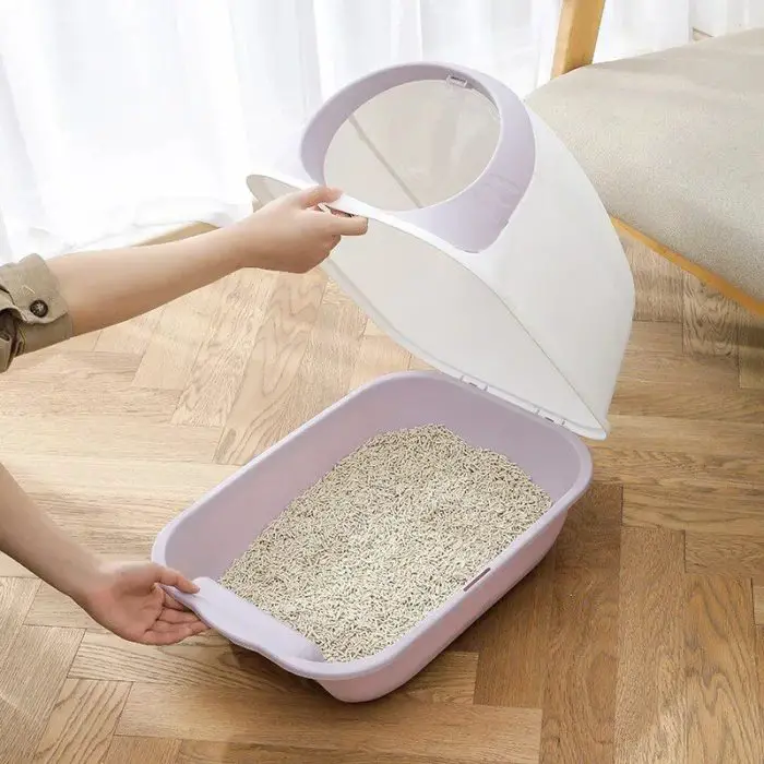 A person is carefully assembling the 12586-f9011d cat litter box on a wooden floor.