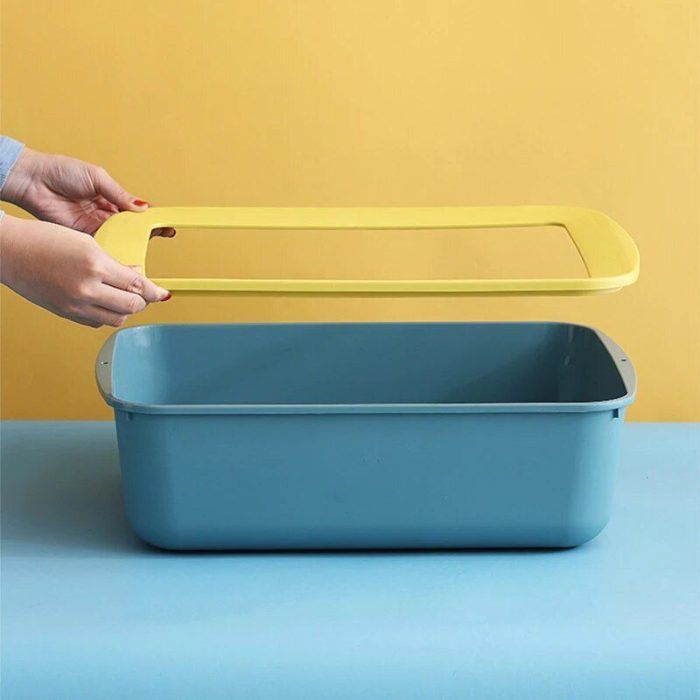 A person is placing a yellow lid onto a rectangular blue container, reminiscent of a cat litter box, against a yellow background, as shown in the image 12589-fd89c4.jpg.