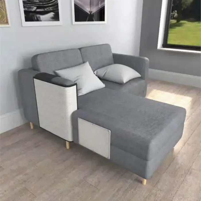 A grey L-shaped sofa with two pillows, listed as "12695-53d5be.jpg," sits in a well-lit room with wooden flooring near a window. The wall behind the sofa features three framed pictures and beside the seat is a discreet cat scratching pad, blending seamlessly into the cozy setting.