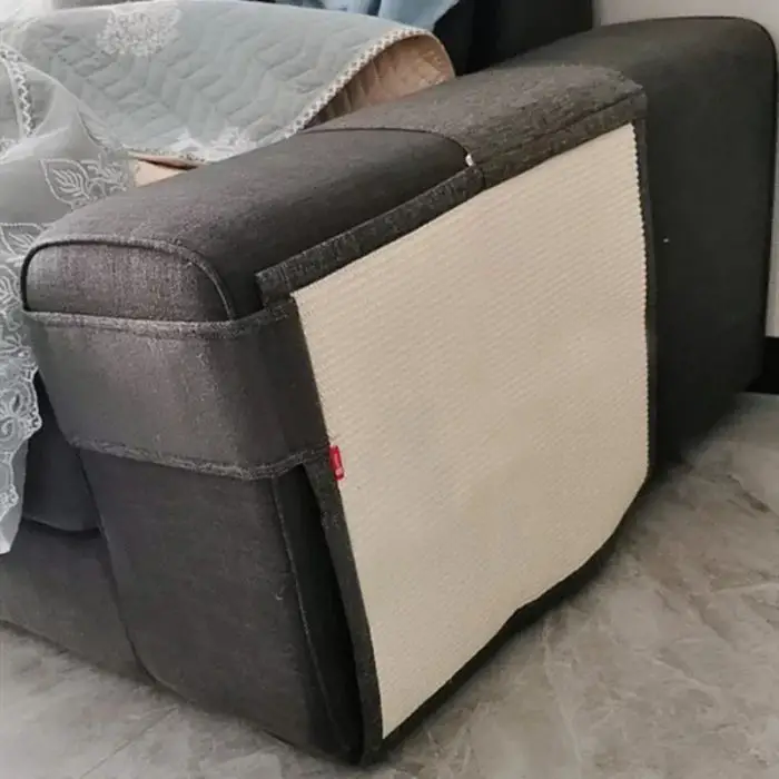 A dark gray couch with a light beige cat scratching pad attached to the side of one armrest and a quilted blanket draped over the back, as seen in product image 12695-a70619.jpg.