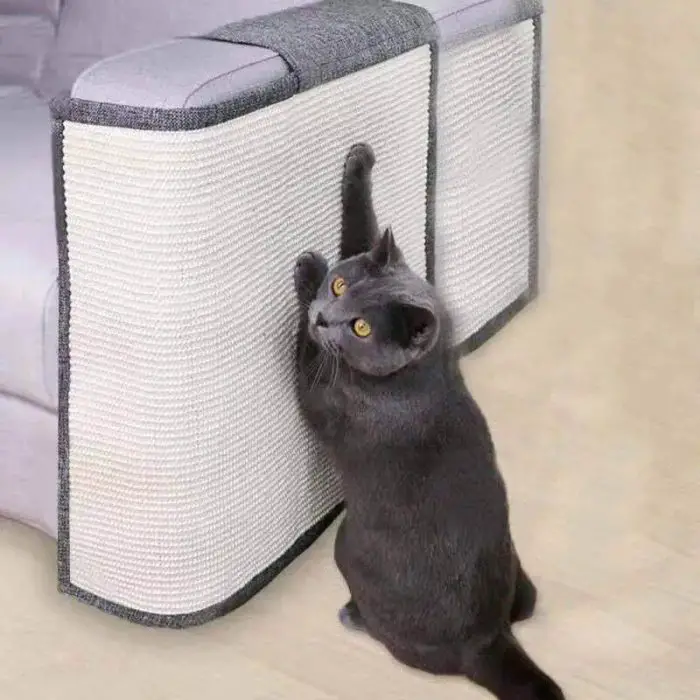 A grey cat scratches a textured white and grey pad, product 12695-c1192c, on the corner of a light grey sofa.