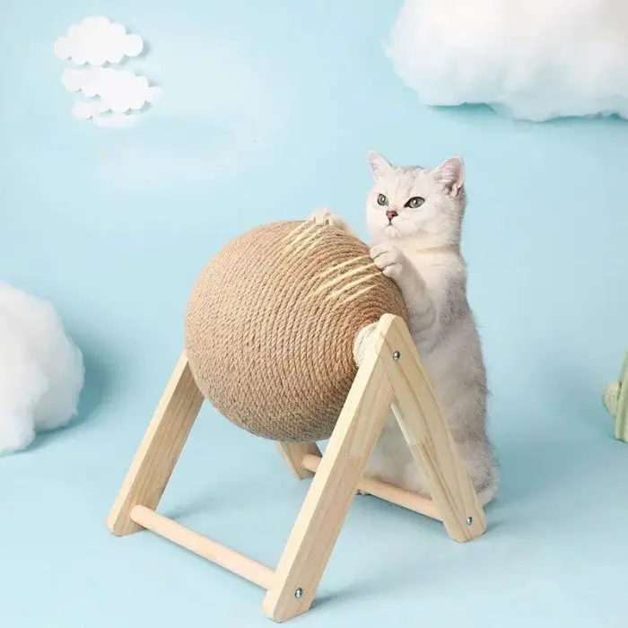 A cat stretches and scratches on the 12730-347a71.jpg Cat Scratching Ball, mounted on a wooden frame, set against a light blue background with decorative clouds.