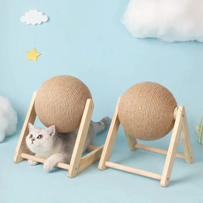 A cat with gray and white fur is lying under a large Cat Scratching Ball mounted on a wooden frame, against a sky blue background featuring clouds and a star. An identical frame sits nearby, both part of the product 12730-54331f.jpg.