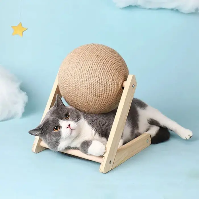 A gray and white cat lies beneath a triangular wooden frame that features a sisal rope Cat Scratching Ball, all set against a blue background adorned with clouds and a star—a scene captured in image 12730-d76350.jpg.