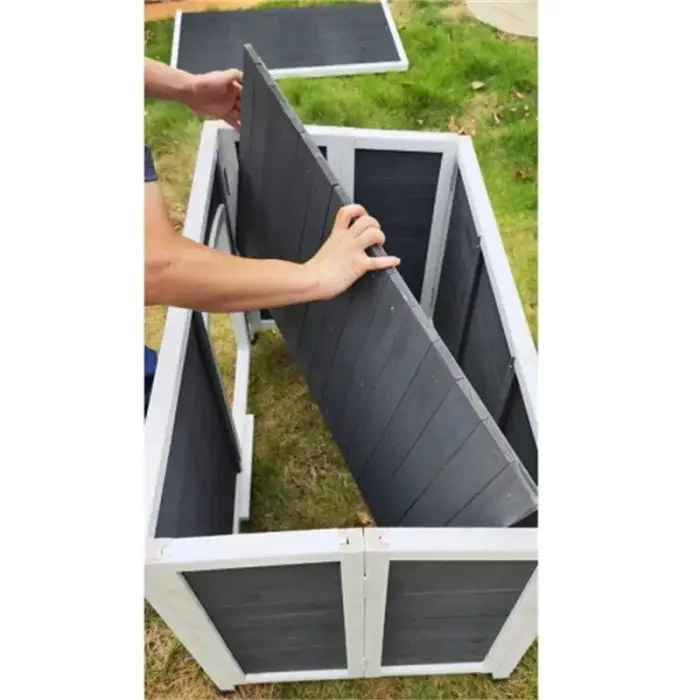 Someone is assembling the 12744-f0cd56.jpg black and white outdoor storage box on grass, placing a panel into the frame. Various parts are scattered around, reminiscent of pieces from a dog house project.