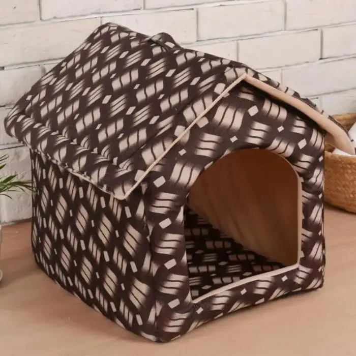 A small, fabric pet house with a brown and beige woven pattern, named 12785-6e88d2.jpg, sits on a wooden surface in front of a white brick wall. This foldable house features a triangular roof and an arched entrance.