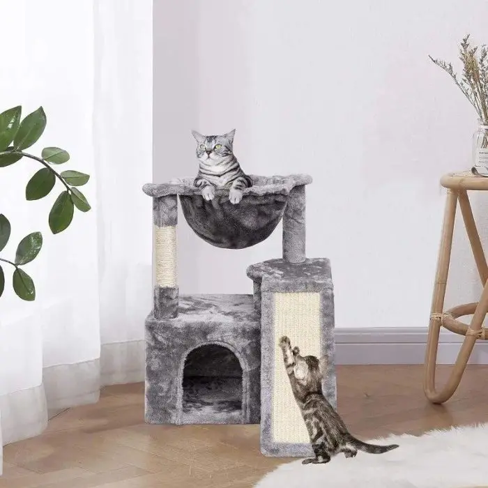 Two cats on a 12807-cf7533.jpg Cat Activity Tower; one is lounging in the hammock while the other is scratching a post. The activity tower is set up in a bright room with white curtains and a nearby plant.