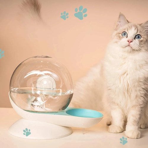 A fluffy white and gray cat sits next to a futuristic cat water fountain with a spherical design from the 12816-541e1b.jpg image. Blue paw prints are visible on the background wall.