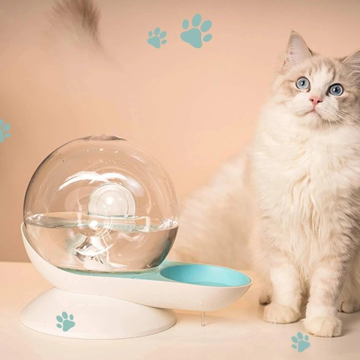 A fluffy white and gray cat sits next to a futuristic cat water fountain with a spherical design from the 12816-541e1b.jpg image. Blue paw prints are visible on the background wall.