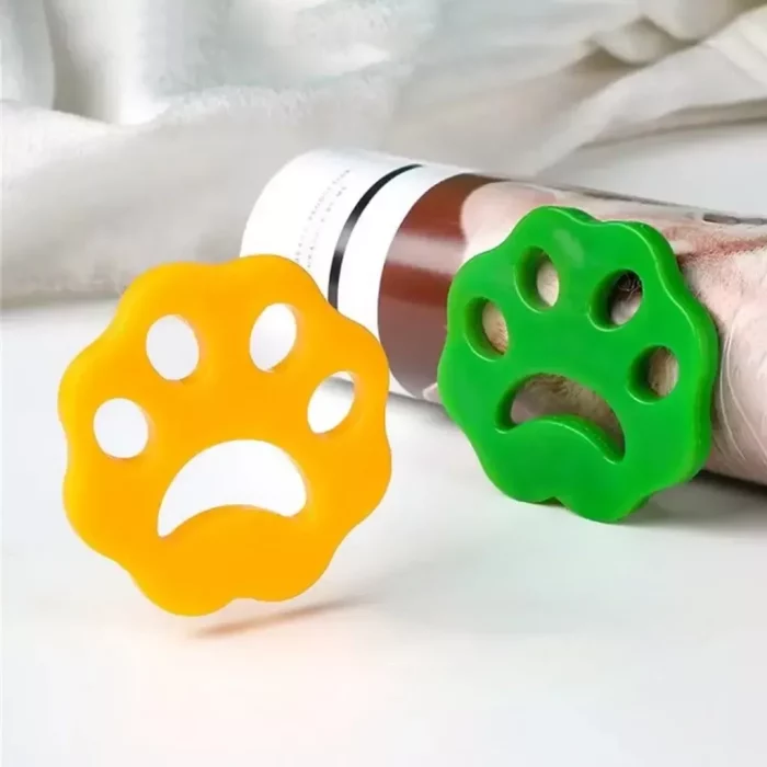 Two reusable silicone, paw-shaped toothpaste tube squeezers, one yellow and one green, are placed on a white surface in front of a partially squeezed tube of 9573-5d88e6.webp.