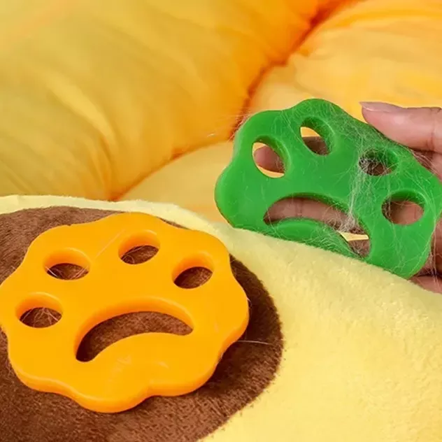 Two **9573-d9d26d.webp**, one orange and one green, made from eco-friendly reusable silicone, are shown with visible pet hair on the green remover, placed on a yellow cushion.