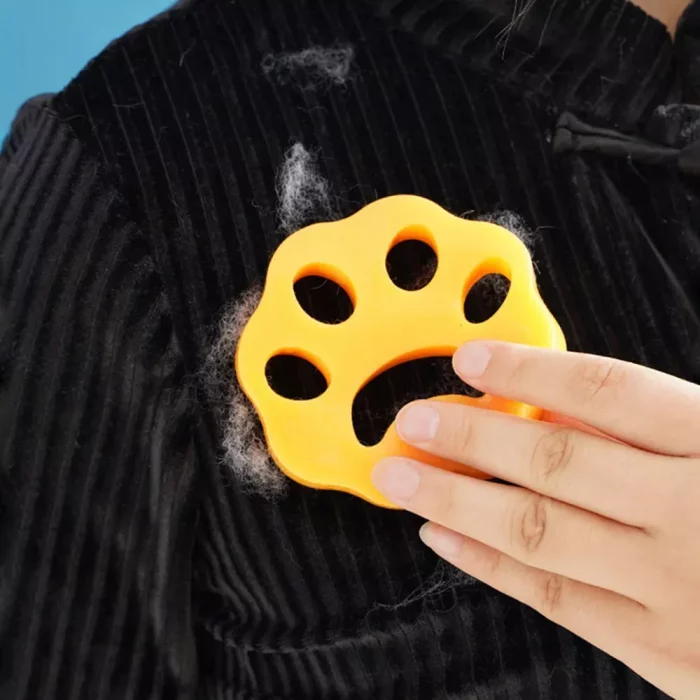 Hand holding a reusable, yellow paw-shaped 9573-fa7355.webp to eliminate pet hair from a black fabric surface.