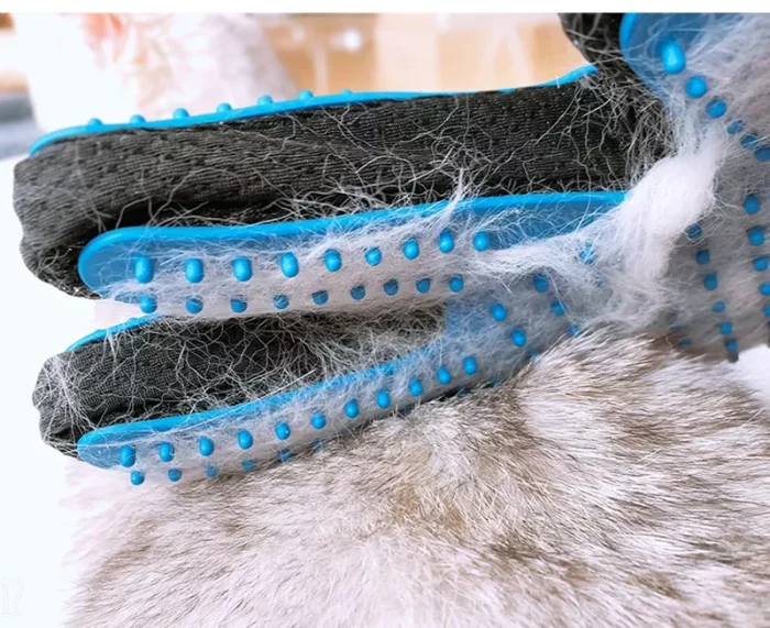 A luxurious pet grooming glove with blue rubber bristles is covered in gray and white fur. The 9591-30ad90.webp is being used to brush an animal with similarly colored fur.