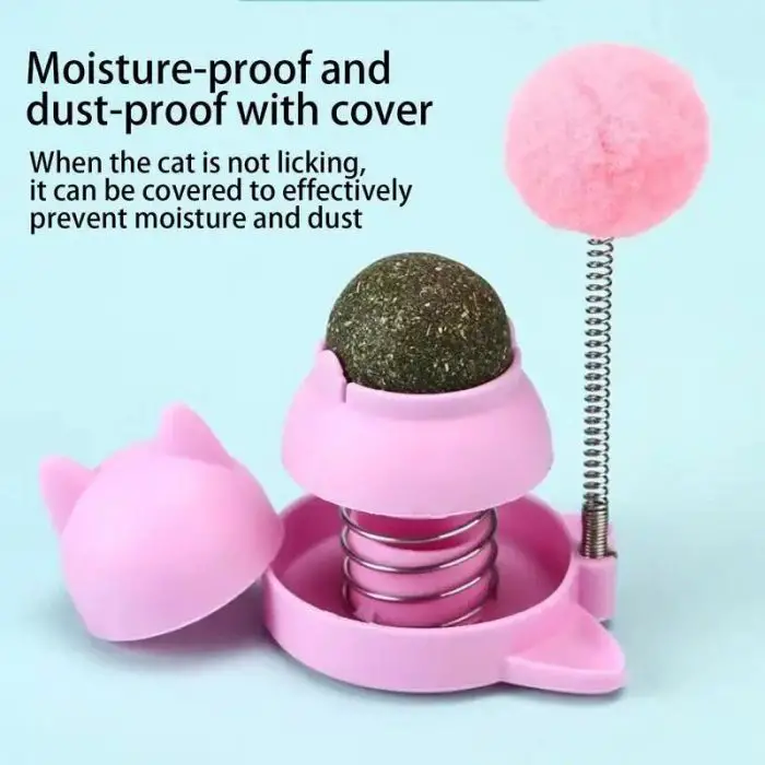 A 9783-67964d.jpg with a removable cover reveals a green ball on a spring. The cover, shaped like cat ears, claims to prevent moisture and dust when the ball is not in use. Attached is a pink pompom and an adhesive catnip ball for added fun.