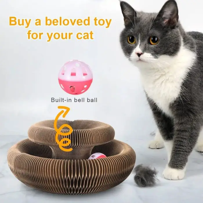 Gray and white cat stands next to a circular brown 9796-390383.jpg with a built-in bell ball. Text above reads, "Buy a beloved cat toy for your cat.