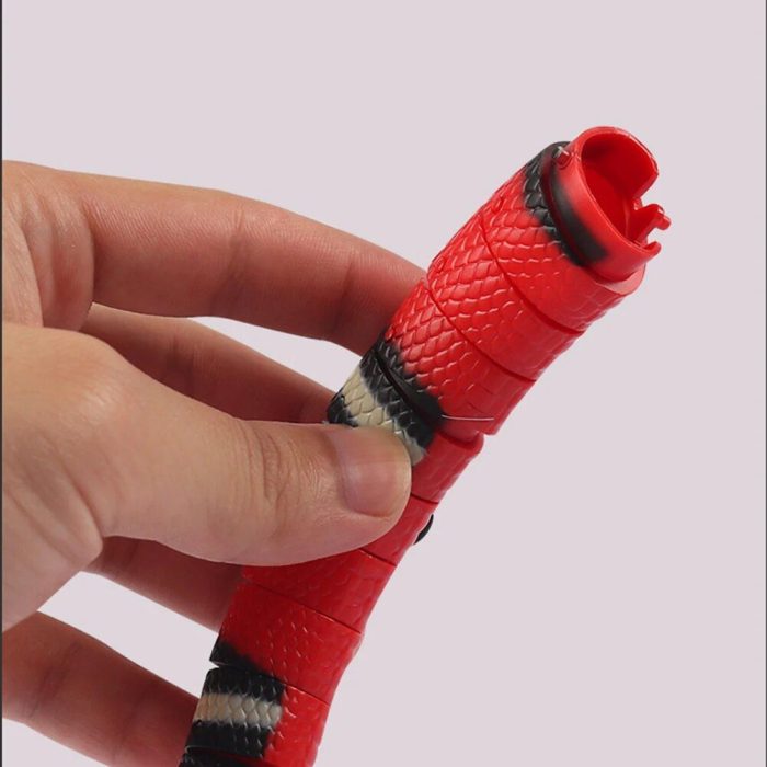 A hand is holding a segmented, flexible, red and black USB rechargeable snake toy with white bands against a plain background. The 9828-aa1309.jpg’s mouth is open at the top.