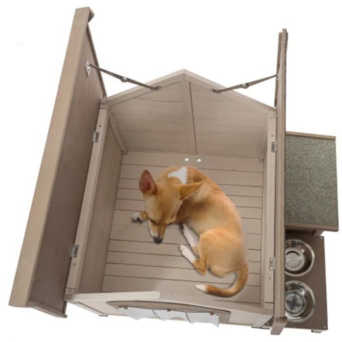 A small tan and white dog is curled up inside a 9869-377dbc.jpg. The doghouse boasts a hinged roof, an attached elevated feeding station with food and water bowls, and a green mat.